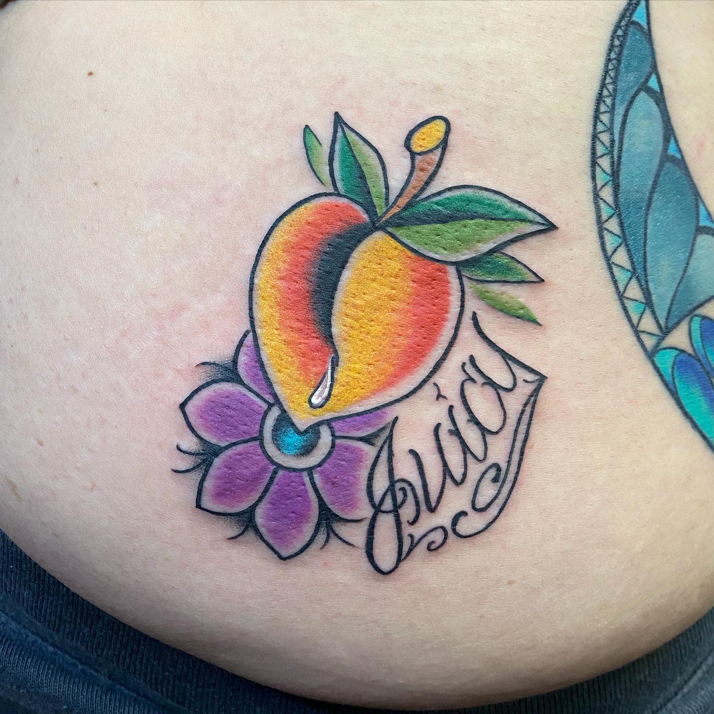 Tattoo of a colorful peach, green leaves, pink flower, and the word "Juicy" on skin